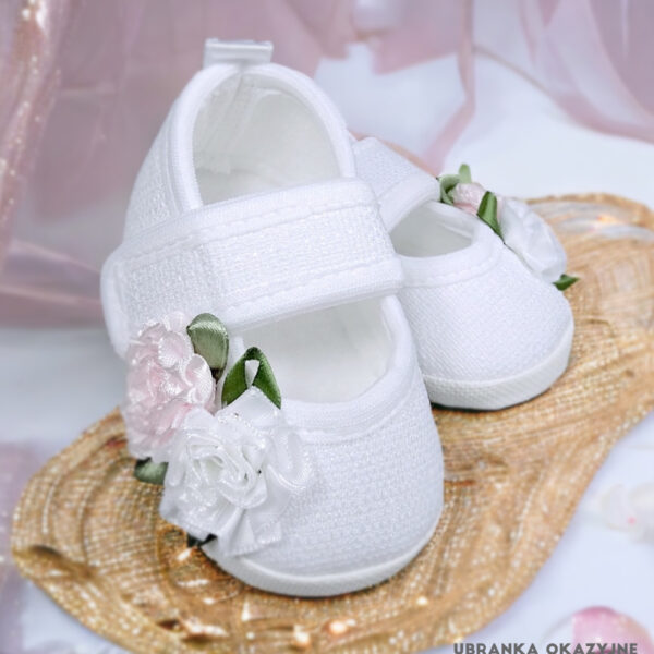 Białe balerinki do chrztu dla niemowlaka ozdobione biało-różowymi kwiatami i zielonymi listkami.