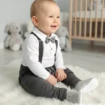 Eleganckie ubranko do chrztu dla chłopca: białe body koszulowe, szara mucha, szelki i spodnie.