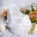 Białe koronkowe balerinki do chrztu dla niemowlaka zdobione cekinami i kwiatkiem