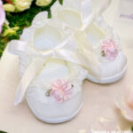 Satynowe balerinki do chrztu dla dziewczynki w kolorze ecru, zdobione koronką i różowym kwiatkiem, wiązane wstążką
