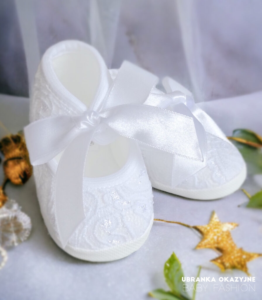 Białe koronkowe balerinki dla niemowlaka do chrztu z dużą atłasową kokardą.
