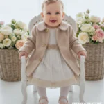 Elegancki beżowy płaszczyk dla dziewczynki do chrztu ozdobiony złotymi kokardkami.