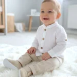 Muślinowy komplet do chrztu dla chłopca – biała koszula ze stójką i beżowe spodnie wizytowe.