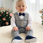 Eleganckie ubranko do chrztu dla chłopca: szara kamizelka i spodnie w niebieską kratę, biała koszula oraz granatowa muszka.