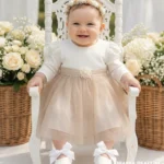 Elegancka sukienka do chrztu dla dziewczynki w kolorze ecru z tiulowym dołem i koronką przy rękawach.