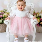 Biało-różowa sukienka do chrztu z tiulowym dołem i ozdobnym kwiatkiem w pasie.