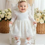 Elegancka koronkowa sukienka do chrztu w kolorze ecru z długim rękawem i tiulowymi detalami na ramionach.