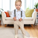 Elegancki komplet do chrztu dla chłopca: beżowe spodnie, białe koszulobody, szelki w kratkę i mucha