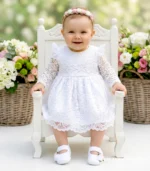 Biała sukienka do chrztu z koronki z długim rękawem i ozdobnymi patkami na ramionach.