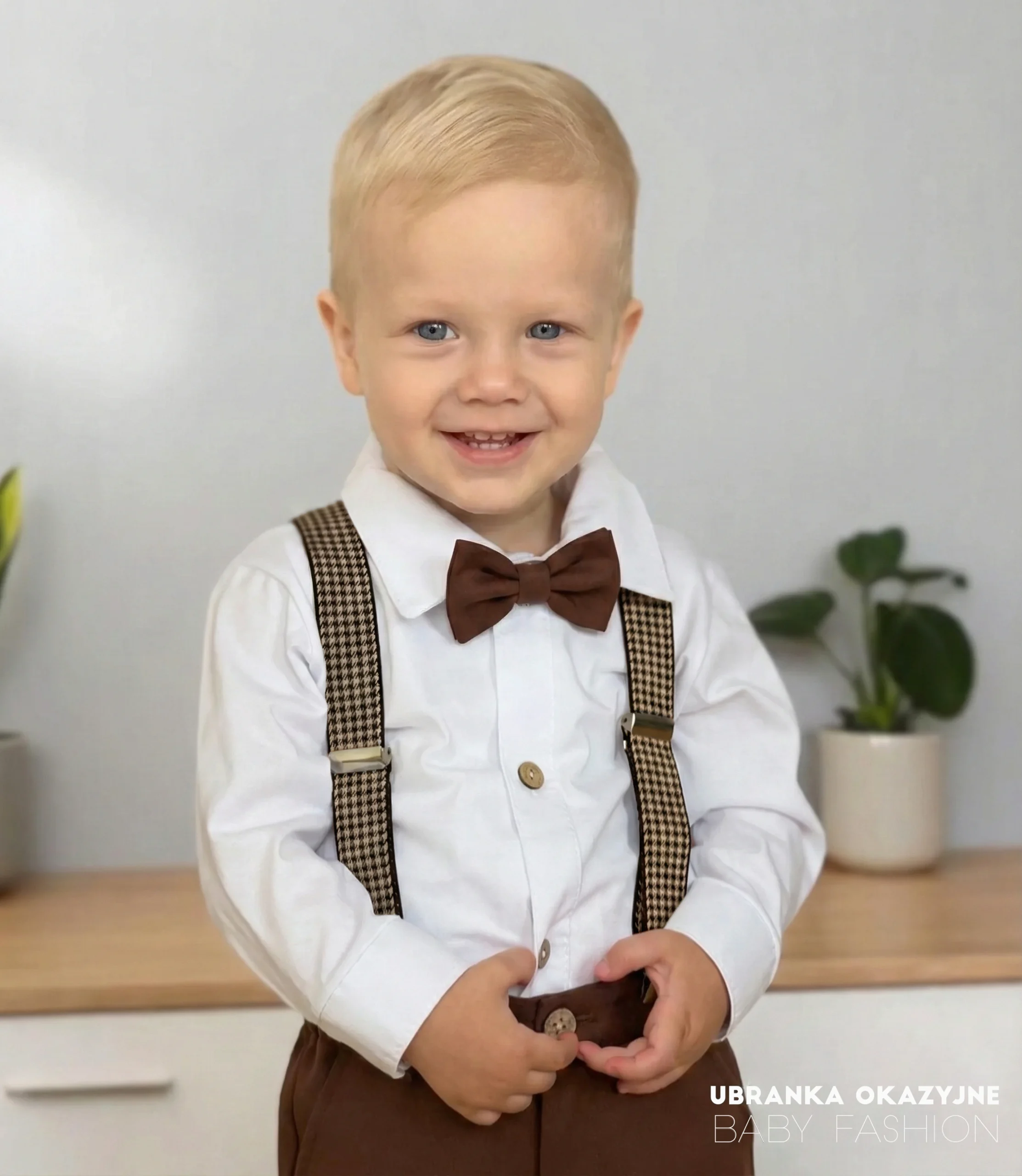 Chłopiec w szelkach w pepitkę i czekoladowych spodniach i czekoladowej muszce