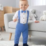 Eleganckie ubranko do chrztu dla chłopca: niebieskie spodnie z szelkami, białe koszulo-body i mucha.